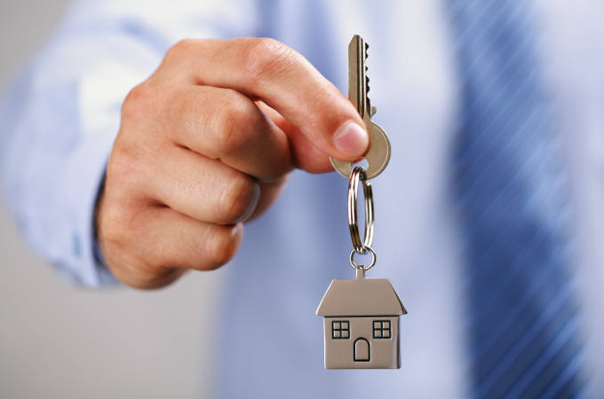 Holding out house keys on a house shaped keychain