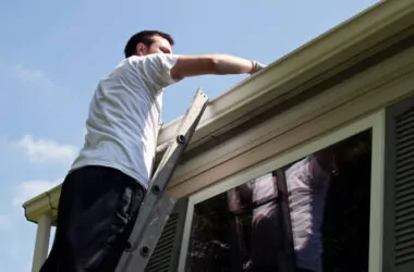 Young man on ladder cleaning house gutters