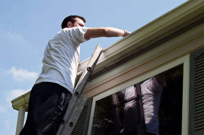 Young man on ladder cleaning house gutters