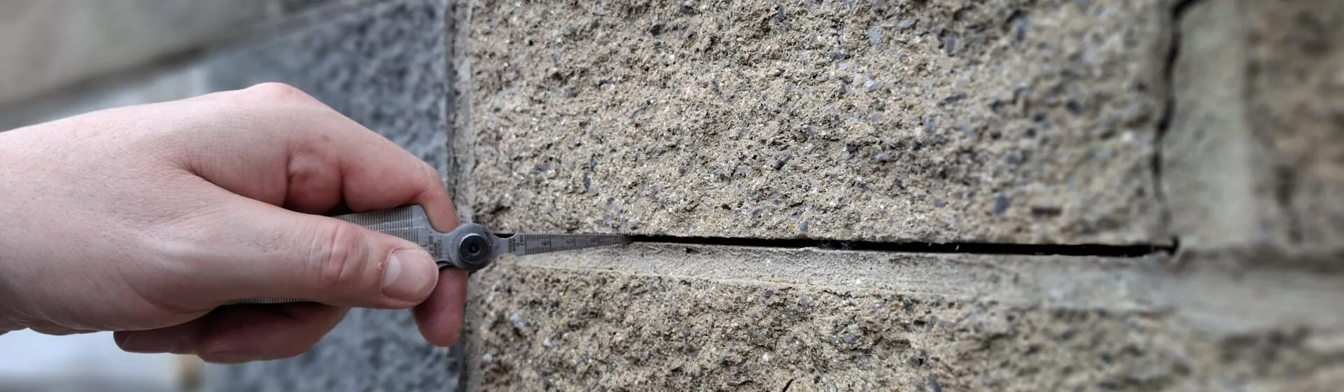 Close-up of a crack in a concrete block wall being measured with a crack width gauge during a structural inspection.